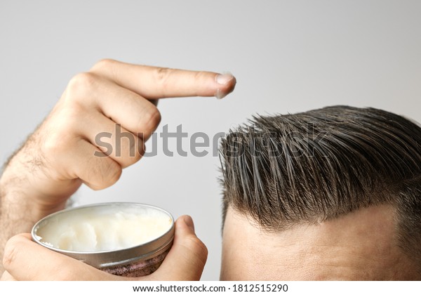 Man applying a clay, pomade, wax, gel or mousse from
round metal box for styling his hair after barbershop hair cut.
Advertising concept of mans products. Treatment and care against
lost of hair