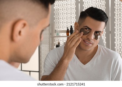 Man Applying Dark Under Eye Patch Near Mirror At Home