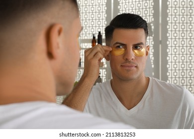 Man applying golden under eye patch near mirror at home - Powered by Shutterstock