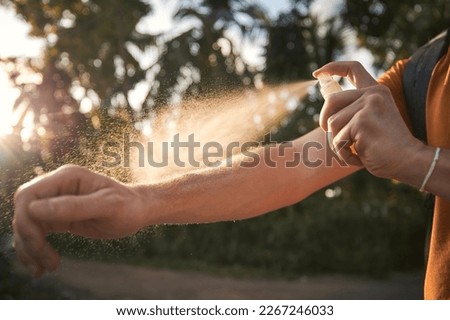 Man is applying insect repellent on his hand against palm trees. Prevention against mosquito bite in tropical destination. 	