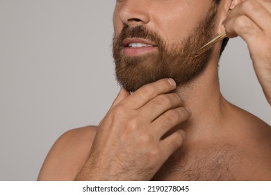 Man Applying Oil Onto Beard On Grey Background, Closeup