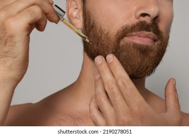 Man applying oil onto beard on grey background, closeup - Powered by Shutterstock