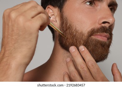 Man Applying Oil Onto Beard On Grey Background, Closeup