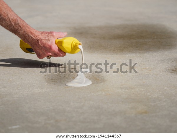 Man applying oil stain remover to concrete
driveway. Removing automobile motor oil stains from parking spots
with cleaning product.