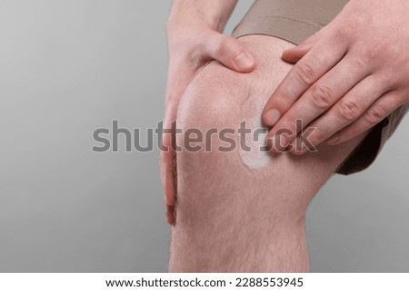 Man applying ointment onto his knee on light grey background, closeup. Space for text