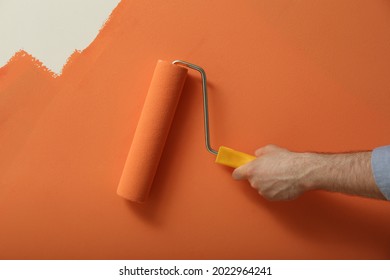 Man Applying Orange Paint With Roller Brush On White Wall, Closeup