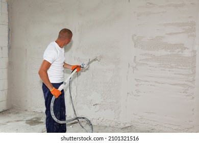 A man is applying stucco on the wall, plastering, coating the wall by spraying stucco with a stucco sprayer.