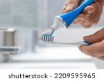 Man applying toothpaste on brush in bathroom, closeup. Space for text