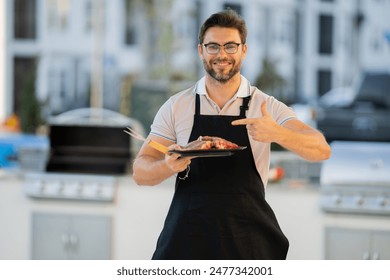 a man in an apron grilling a steak. Barbeque on holiday picnic. Man grilling a steak on BBQ. Grill and barbecue cook. Chef with BBQ cooking tools. Barbecue and grill. Picnic barbecue party. - Powered by Shutterstock