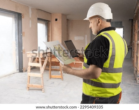 Man architect. Guy in unfinished building. Construction company contractor. Architect with construction drawings. Foreman is holding tablet. Architect man in yellow vest. Businessman engineer