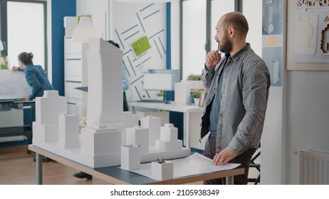 Man architect taking notes on blueprints plan to design building structure and model. Industrial contractor creating construction layout and working on project strategy with maquette.