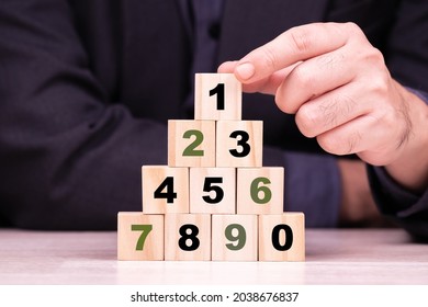 Man Arranges The Number Wood Cubes From 0-9 As A Pyramid, With The First One On The Top, Step By Step To Success, The Process To Achieve, Ranking, Or Mathematics And Calculation Concept