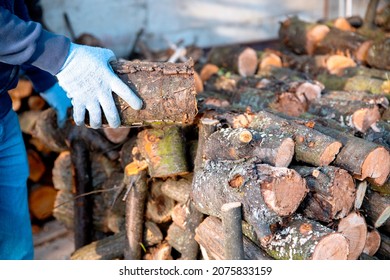 Man arranging wood logs on stack. Split cut firewood to dry. 
				Male hands stacking logs of different lengths in the firewood store