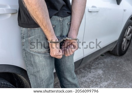 MAN ARRESTED AND HANDCUFFED BY THE POLICE ON THE STREET NEXT TO A CAR. REAR VIEW. Foto d'archivio © 