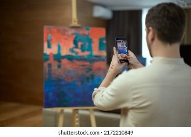 Man artist takes pictures by phone masterpiece of modern art, contemporary abstract painting for social media, rear view