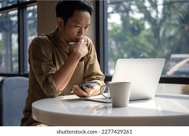 man asian working laptop computer and smartphone on desk focused on his work, with a serious expression on his face.