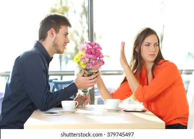 Man asking for forgiveness offering a bunch of flowers to his girlfriend in a coffee shop with an exterior background. Couple problems concept