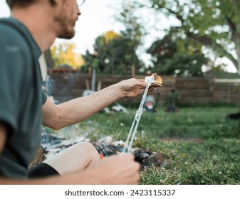Man assembles s’more with campfire behind