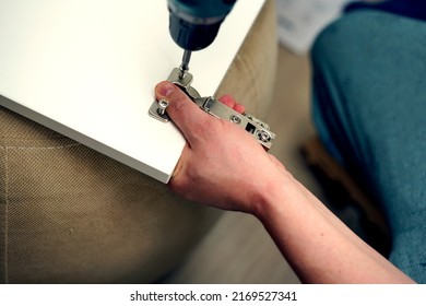 A man assembles furniture, screwing hinges to a wooden door with a screwdriver