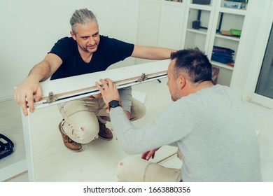 A Man Is Assembling A Bathroom Cabinet With His Brother