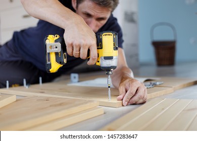 Man Assembling Furniture At Home Using A Cordless Screwdriver