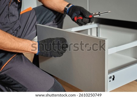 Man assembling kitchen drawer in modern cabinet using screwdriver. Handyman installing and adjusting drawer slide mechanism in contemporary kitchen. Furniture installation