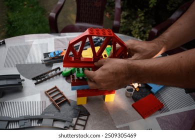 A man assembling lego bricks on a garden table with colourful tablecloth in a garden.
