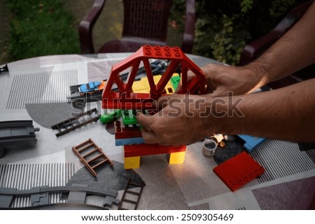 A man assembling lego bricks on a garden table with colourful tablecloth in a garden.
