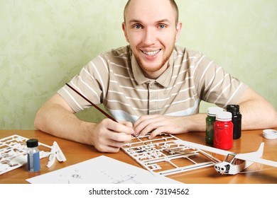 Man Assembling Plastic Airplane Model And Painting Pieces, Smiling, Looking At Camera