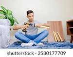Man assembling a small wooden table as part of a DIY home decor project. He is using an electric screwdriver to drive a screw into a wooden leg to attach it to the table