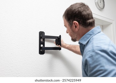 a man is assembling a TV bracket. He keeps instructions and is focused on the process. There are parts and tools nearby. Application: DIY, instructions, repair, TV accessories.