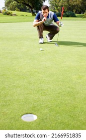 Man assessing his options to putt. Full length of man crouching on the putting green and assessing his options to putt the ball.