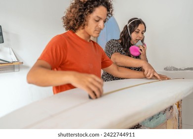 Man and assistant measures the length of a surfboard with a measuring tape in a repair workshop - Powered by Shutterstock