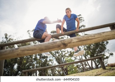 Man assisting woman to climb a hurdles during obstacle training at boot camp - Powered by Shutterstock