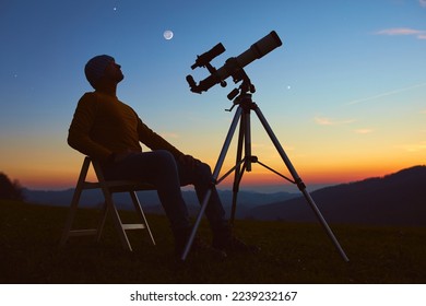 Man with astronomy telescope looking at the night sky, stars, planets, Moon and shooting stars. - Shutterstock ID 2239232167