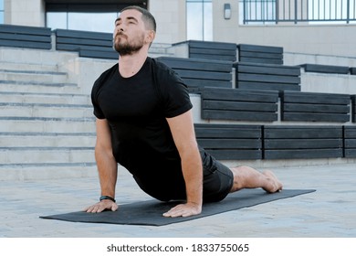 Man athlete in black sportswear practices yoga exercises in cobra pose outdoors. - Powered by Shutterstock