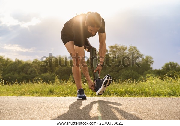 Man\
athlete with leg prosthesis tying his shoes outdoors - ready for\
tryout- people with disabilities lifestyle concept\
