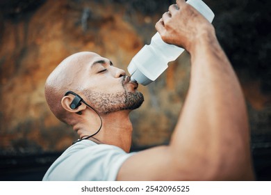 Man, athlete rest and outdoor to drink water, profile and earphones for music with exercise. Male person, h2o and cardio break with sports beverage, nutrition and mineral liquid on mountain road - Powered by Shutterstock