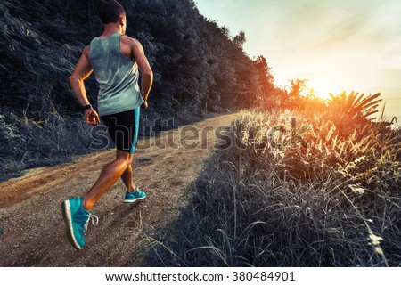 Man athlete running on the gravel road with green grass and trees on its sides