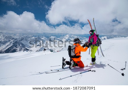 A man athlete skier freerider makes a proposal to marry his woman skier high in the mountains in winter. against the backdrop of snow-capped peaks. Wedding proposal in extreme conditions