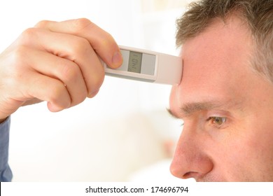 Man Attempting To Measure Body Temperature With Thermometer On Forehead