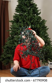 A Man Attempts To Untangle A String Of Christmas Lights In Front Of An Undecorated Christmas Tree.