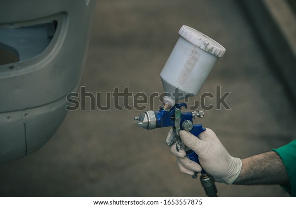 Man with automotive air spray gun in action during\
the restoration of a vintage car. Applying first base layer of\
paint onto bare metal.
