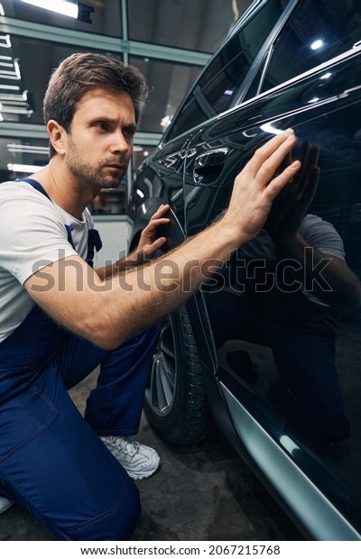 Man\
automotive technician looking for scratches on\
car