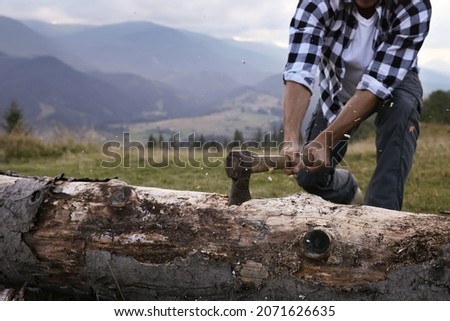 Man with axe cutting tree log in mountains, closeup