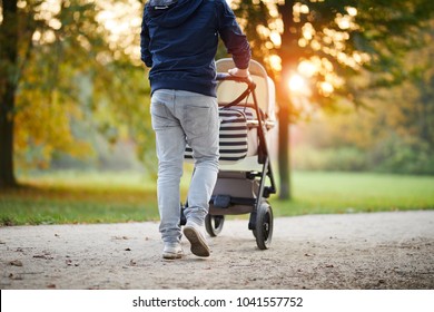 Man With Baby Stroller Walks In The Autumn Park At Sunset