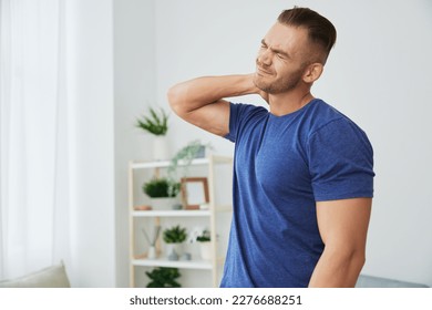 Man back neck and shoulder pain, inflammation of muscles and ligaments rupture during sports, inflammation and injury, in a blue t-shirt at home - Shutterstock ID 2276688251