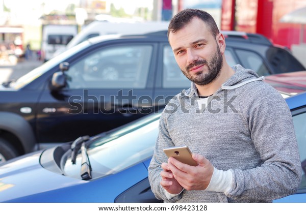 Man in the background\
of a car with a phone in his hands. Call the car through the\
Internet taxi service.