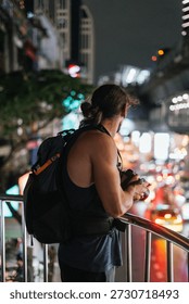 Man with backpack and camera observing night city traffic from a railing