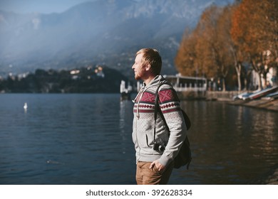 man with a backpack and camera stands on the shore of a mountain lake Como